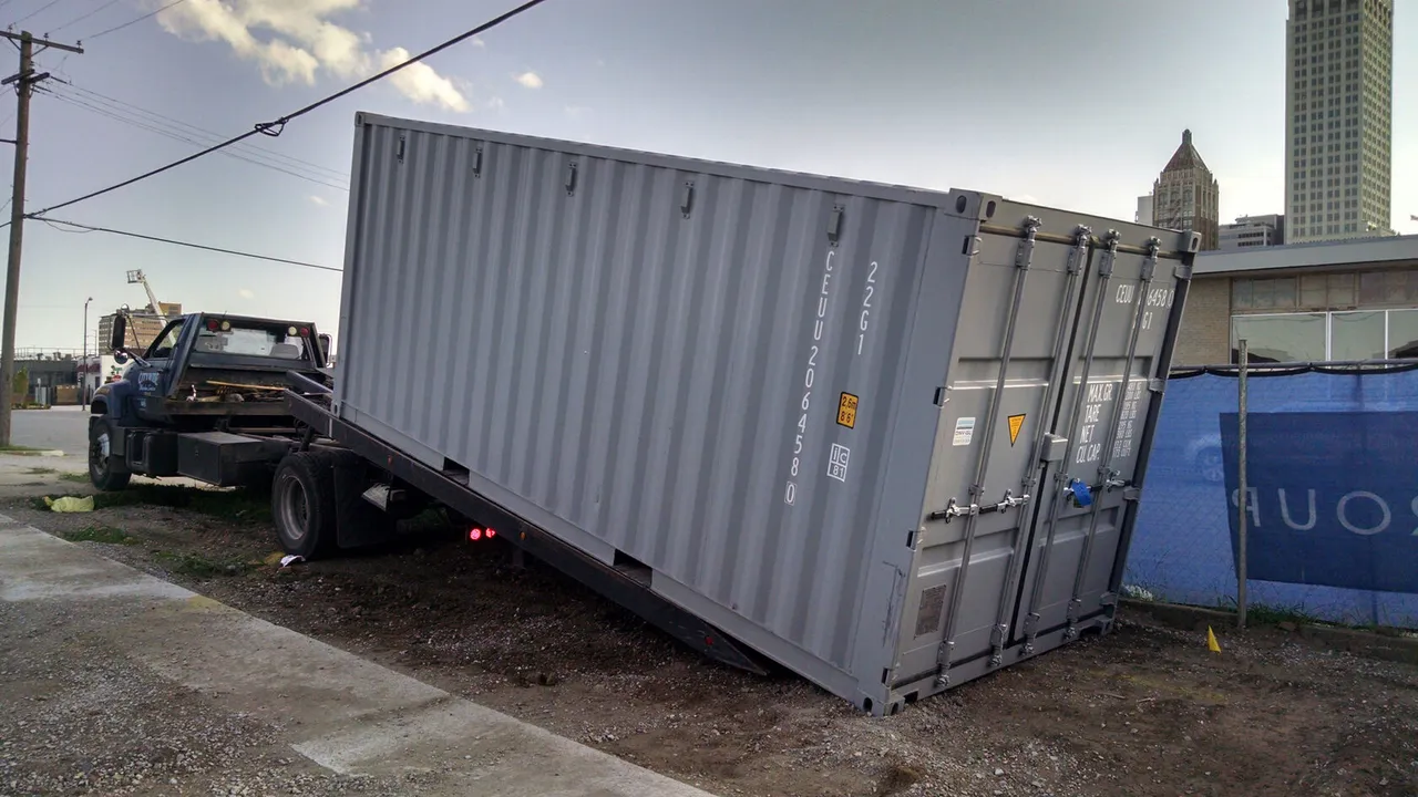Shipping container delivered by tilt-deck truck to a site